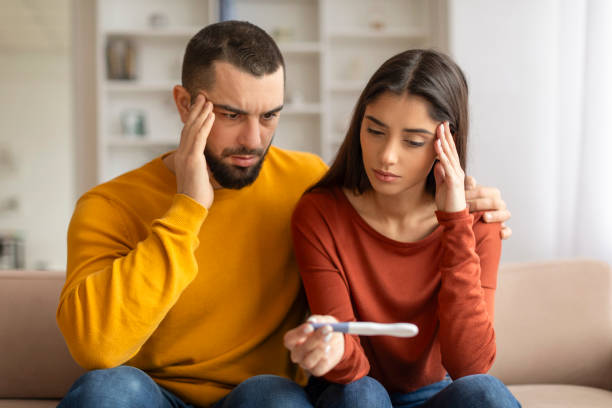 Portrait Of Upset Young Spouses Looking At Negative Pregnancy Test, Suffering Infertility Problems, Depressed Millennial Couple Sitting Together On Couch At Home, Having Health Issues, Closeup Shot